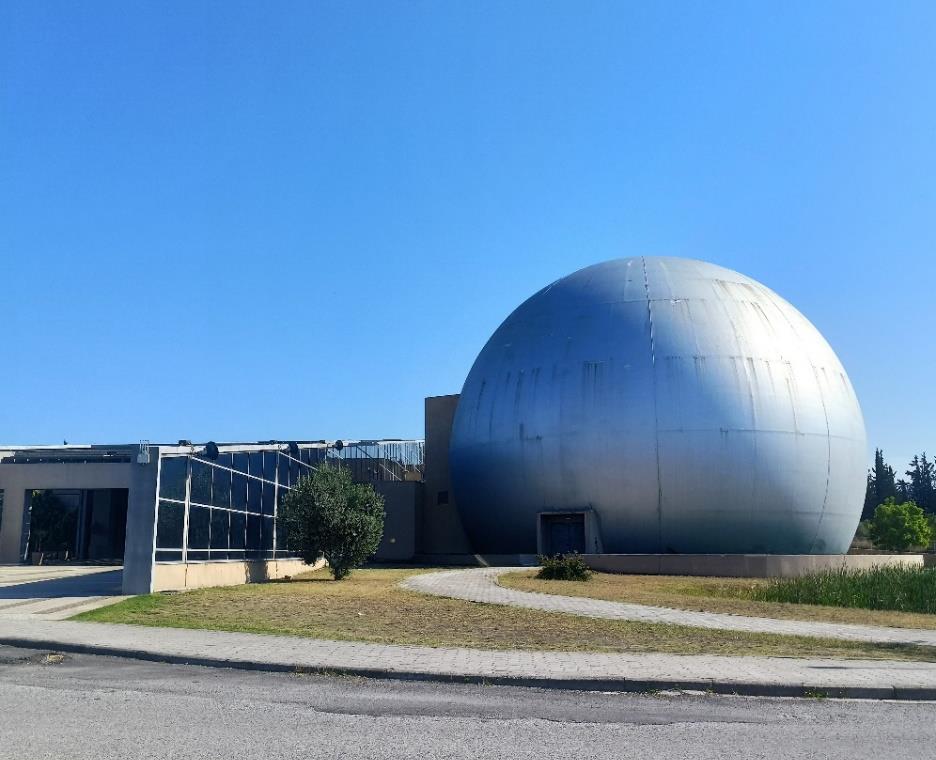 The NOESIS building in Thessaloniki, with its large silver planetarium dome, under a clear blue sky.